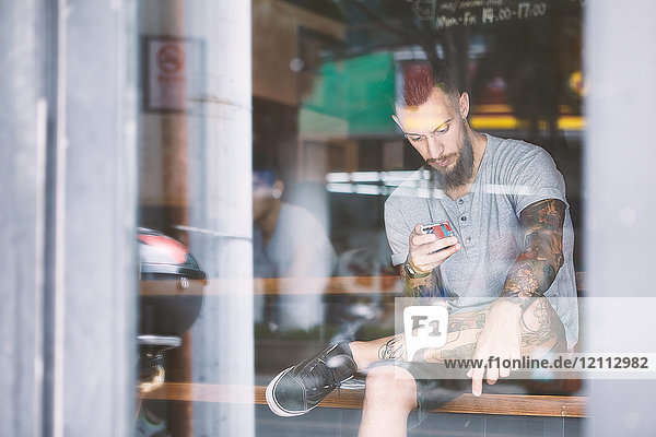 Junger männlicher Hipster im Fensterplatz eines Cafés mit Blick auf ein Smartphone  Shanghai French Concession  Shanghai  China