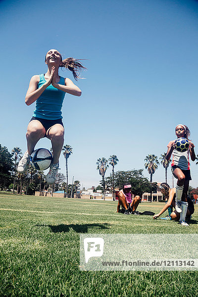 Schulmädchen springt mit Fussball auf Schulsportplatz