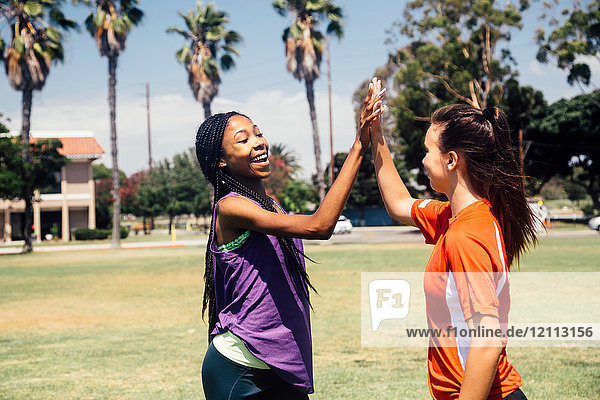 Two teenage soccer schoolgirls high fiving on school sports field