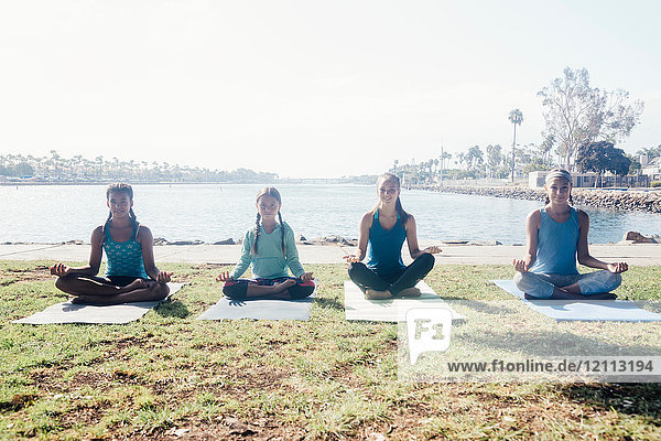 Schulmädchen  die Yoga-Lotus-Pose praktizieren  stellen sich am Seeufer auf dem Schulsportplatz