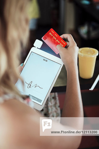 Über-Schulter-Ansicht einer jungen Frau mit digitalem Tablett und Kreditkarte
