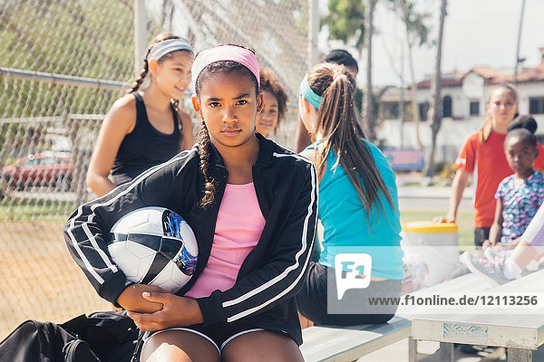 Porträt einer Schülerin in einer Gruppe  die einen Fussball auf dem Schulsportplatz hält