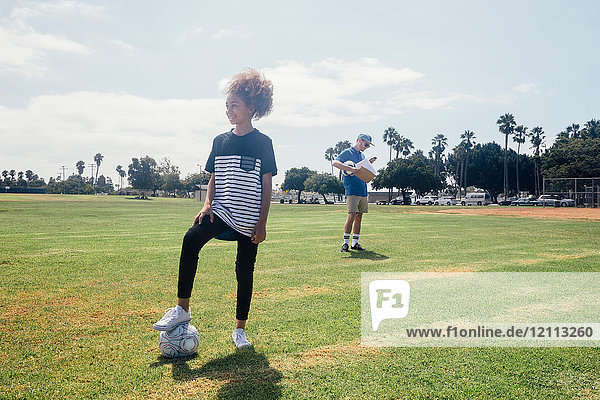 Portrait of schoolgirl with foot on soccer ball on school sports field