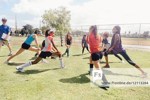 Teacher instructing schoolgirl soccer players in warm up on school sports field