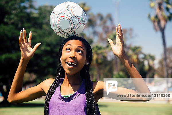 Teenager-Schülerin Fussballspielerin balanciert Ball auf Kopf auf Schulsportplatz