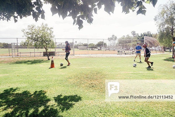 Männlicher Lehrer übt mit Schulmädchen auf dem Schulsportplatz Fussball