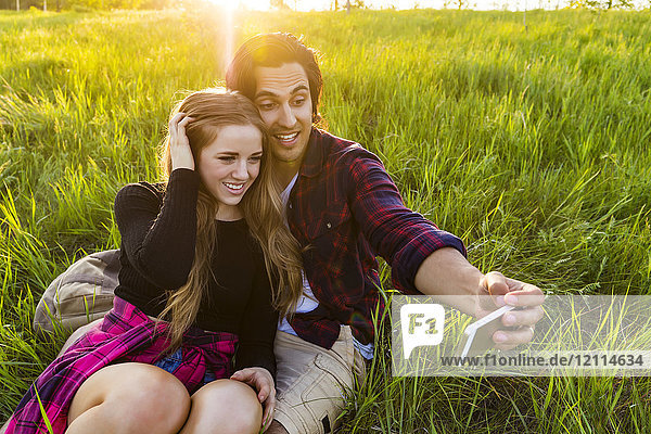 Junges Paar in einem Park  das für ein Selbstporträt mit seinem Mobiltelefon posiert; Edmonton  Alberta  Kanada