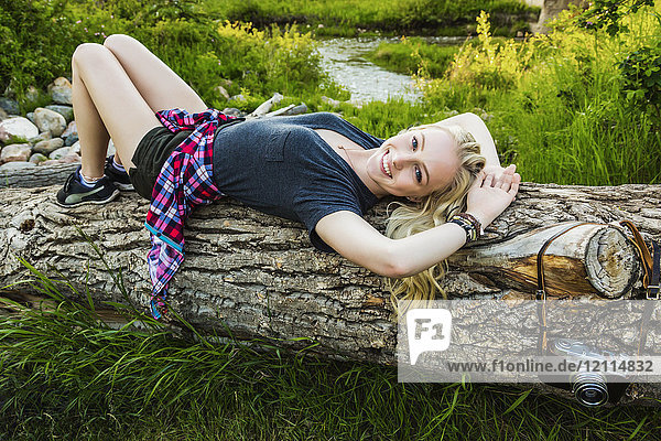 Porträt einer jungen Frau mit langen blonden Haaren  die auf einem Baumstamm in einem Park liegt; Edmonton  Alberta  Kanada