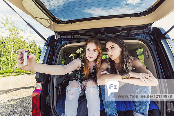 Zwei junge Frauen auf einer Autoreise sitzen auf dem Rücksitz eines Fahrzeugs und machen ein Selbstporträt mit einem Smartphone; Edmonton  Alberta  Kanada