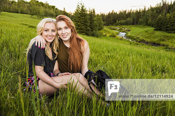 Zwei Freundinnen sitzen umarmt auf einer Wiese und posieren für ein Porträt bei Sonnenuntergang; Edmonton  Alberta  Kanada