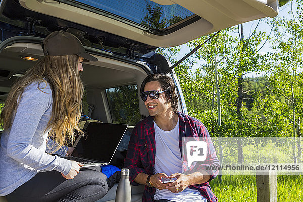 Junges Paar  das in seinem Fahrzeug mit geöffneter Heckklappe auf einen Laptop schaut; Edmonton  Alberta  Kanada