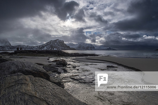A landscape with rugged mountains and sand along the coastline under a cloudy sky; Nordland  Norway