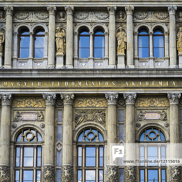 Ornate facade of a building with pillars and statues beside windows with reflection of the blue sky; Budapest  Budapest  Hungary