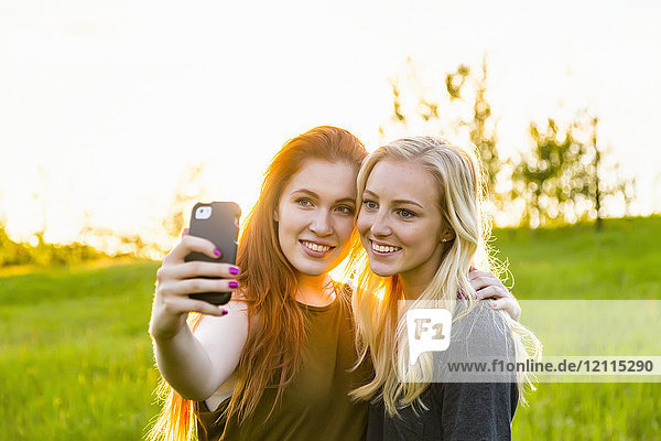 Zwei Freunde stehen in einem Park und machen ein Selbstporträt mit einem Smartphone in der Abenddämmerung; Edmonton  Alberta  Kanada