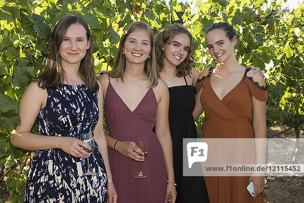 Portrait of four young women dressed in formal wear and holding glasses with drinks; Cobble Hill British Columbia Canada