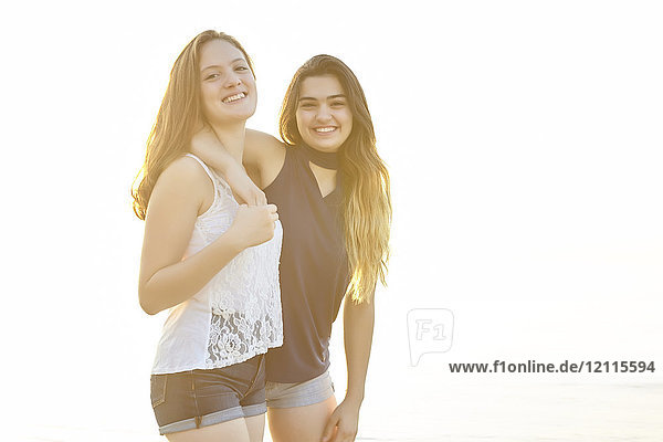 Two teenage girls posing for the camera as they stand in an embrace and bathed in warm sunlight  Woodbine Beach; Toronto  Ontario  Canada