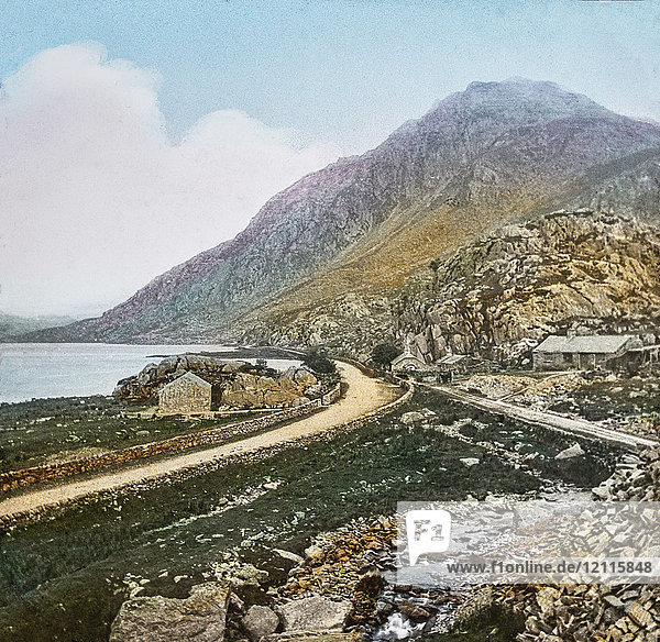 Magic Lantern slide circa 1900 hand coloured. created in 1887. A tour of North Wales. 16 Ogwen Lake.—This is a beautiful sheet of water a mile in length  and is surrounded by the noblest of mountains. The scenery around is bleak and bare in the extreme  and the stillnessand barrenness is appalling. “There sometimes doth a leaping fish Send through the tarn a lonely cheer ;The crags repeat the raven’s croak In sympathy austere. The fishing is very good and quite open to the public. Eels and trout abound.