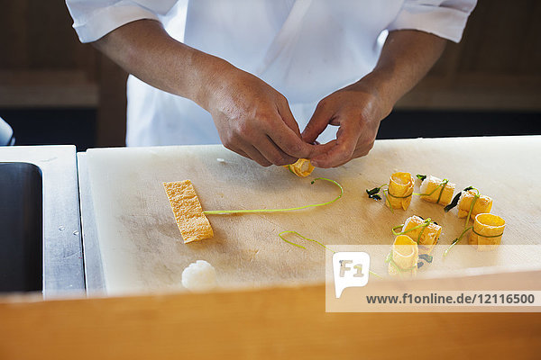 Nahaufnahme aus der Vogelperspektive eines Küchenchefs  der an der Theke eines japanischen Sushi-Restaurants arbeitet und Tofu-Rollen zubereitet.