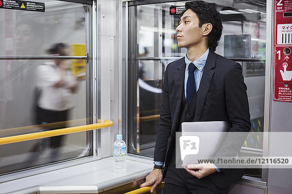 Businessman wearing suit standing on a commuter train  holding laptop.