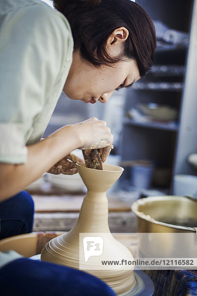 Woman working in a Japanese porcelain workshop  sitting at a potter's wheel  throwing bowl.