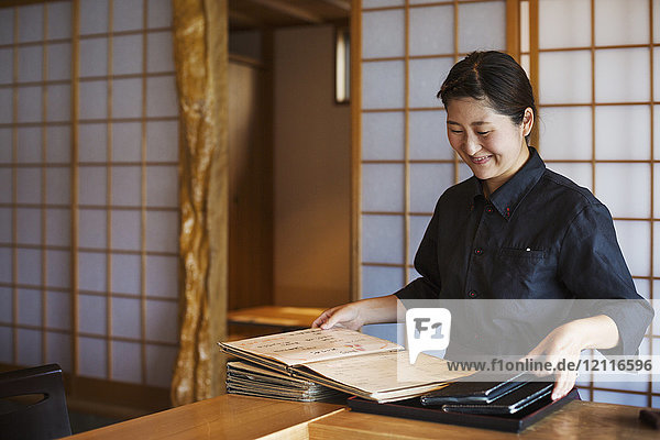 Lächelnde Kellnerin  die an einem Tresen in einem japanischen Sushi-Restaurant steht und Speisekarten hält.