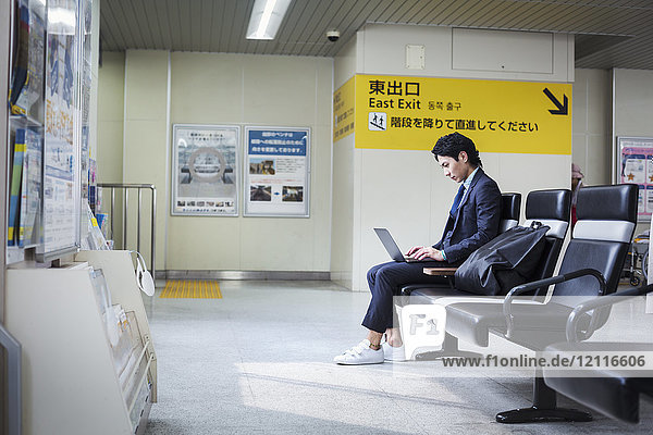 Businessman wearing suit sitting at train station  working on laptop.