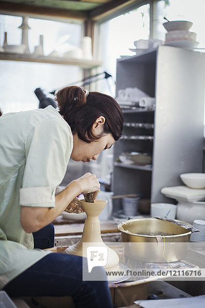 Frau  die in einer japanischen Porzellanwerkstatt arbeitet  an einer Töpferscheibe sitzt und Schüssel wirft.
