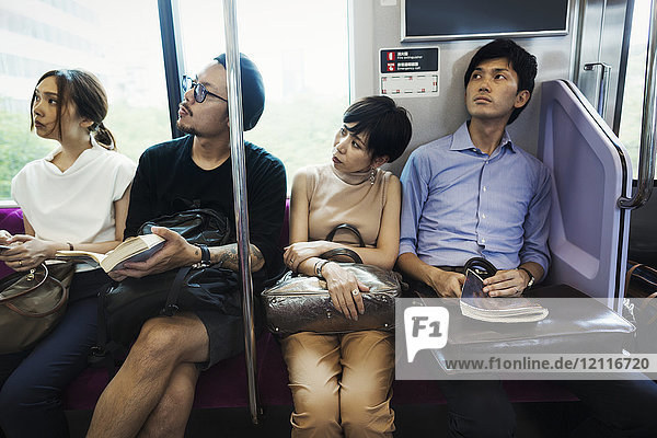 Four people sitting sidy by side on a subway train Tokyo commuters.