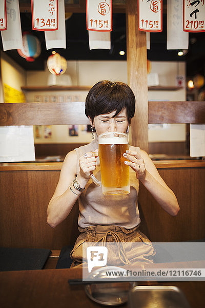 Woman sitting at a table in a restaurant  drinking from large glass of beer.