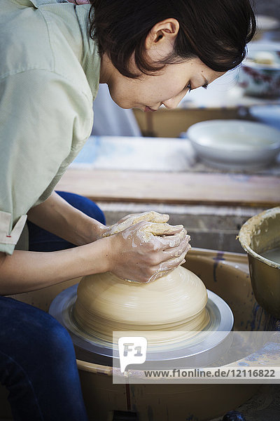 Woman working in a Japanese porcelain workshop  sitting at a potter's wheel  throwing bowl.