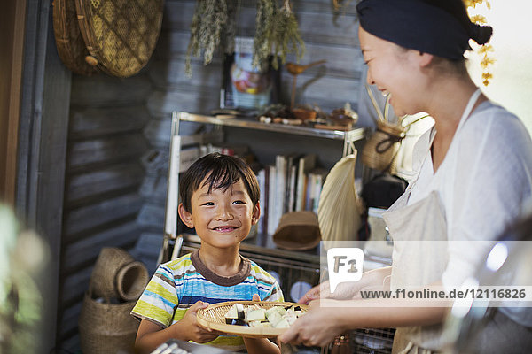 Lächelnde Frau und Junge stehen in einer Küche und halten einen Teller mit Essen in der Hand.