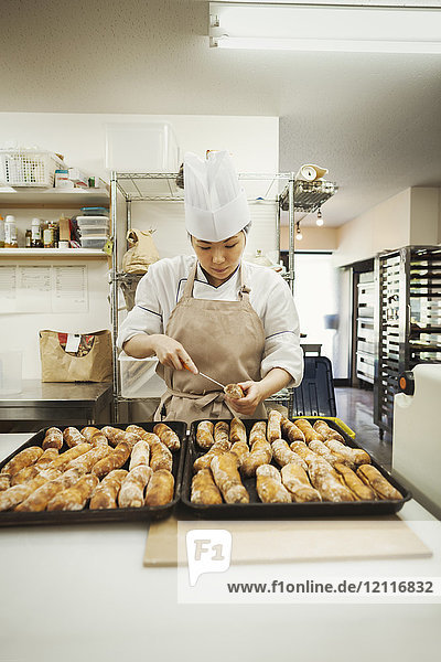 Woman wearing chef's hat and apron working in a bakery  preparing freshly baked rolls on large trays.