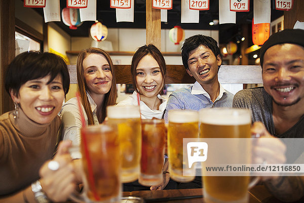 Fünf Personen sitzen seitlich nebeneinander an einem Tisch in einem Restaurant und halten große Gläser mit Bier.