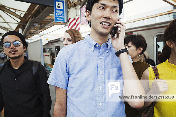 Kleine Gruppe von Menschen  die auf dem Bahnsteig einer U-Bahn-Station stehen  Pendler aus Tokio  Mann mit Smartphone.