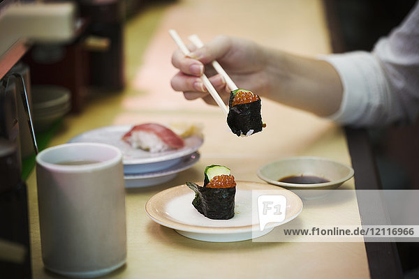 Nahaufnahme einer Person  die in einer Sushi-Bar isst  mit Sushi-Zug  Kaiten-zushi.