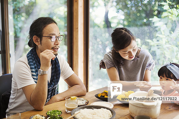 Man  woman and young girl sitting round a table with bowls of food  eating together.