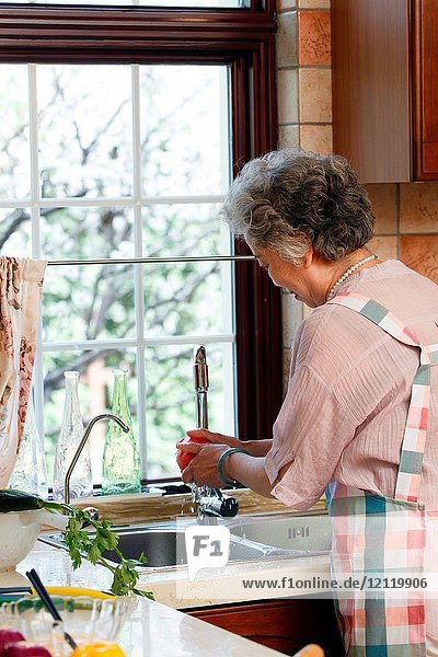 The old woman is washing vegetables in the kitchen