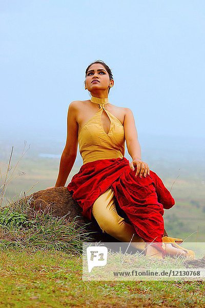 Young woman in Indian dress with hill backdrop looking at the sky.