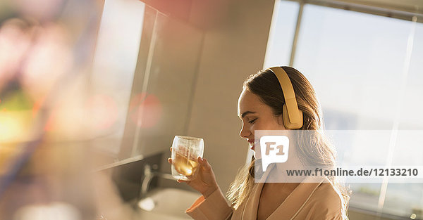 Lächelnde Frau mit Kopfhörern  die Musik hört und trinkt