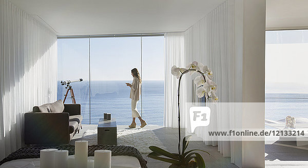 Frau steht auf dem Balkon eines modernen Luxushauses mit sonnigem Meerblick