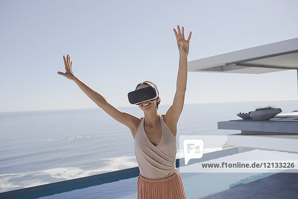 Energetische Frau  die eine Virtual-Reality-Simulator-Brille auf einer modernen  luxuriösen Wohnung mit Blick auf das Meer benutzt