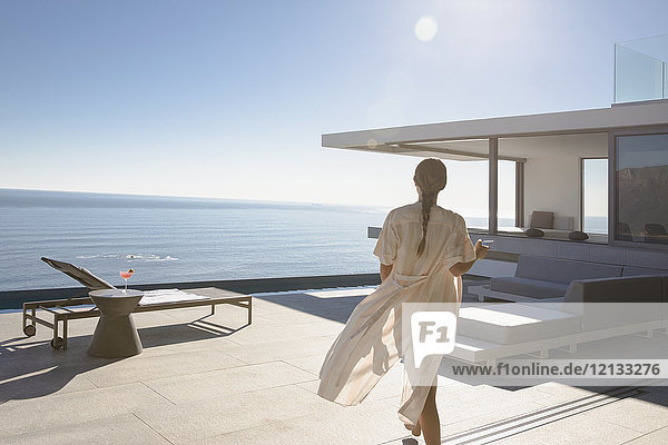 Frau  die auf einer sonnigen  modernen  luxuriösen Wohnung spazieren geht  die eine Außenterrasse mit Meerblick aufweist