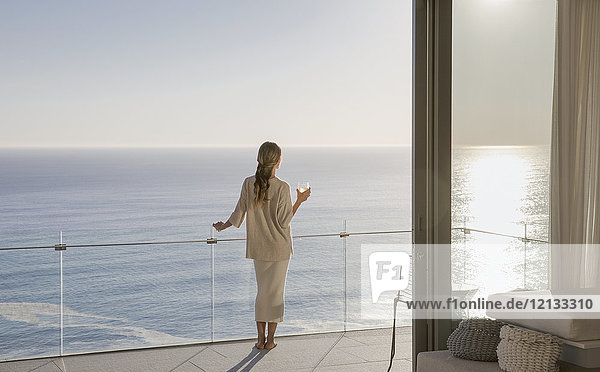 Frau auf sonnigem Luxusbalkon mit Meerblick stehend