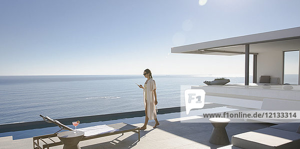 Frau  die auf der sonnigen  modernen  luxuriösen Musterhaus-Terrasse mit Meerblick spazieren geht