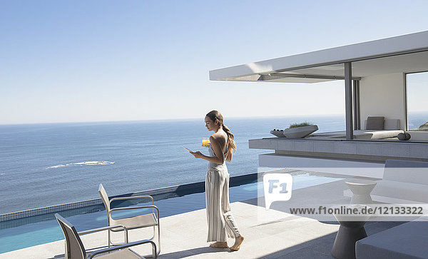 Frau  die mit ihrem Smartphone auf einer sonnigen  modernen  luxuriösen Terrasse mit Meerblick spazieren geht und SMS schreibt