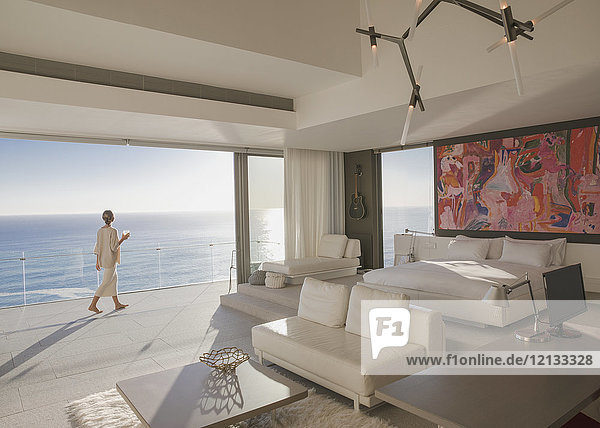 Frau zu Fuß auf sonnigen modernen  luxuriösen Haus Showcase Schlafzimmer Balkon mit Meerblick