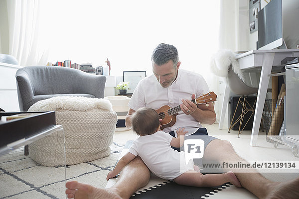 Vater sitzt auf dem Boden und spielt Ukulele für seinen kleinen Sohn