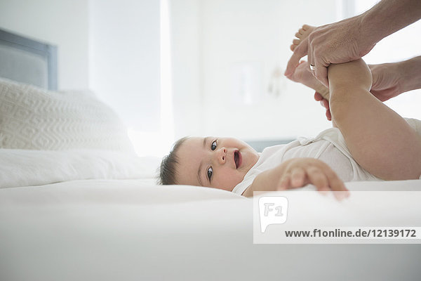 Father holding legs of baby son on bed