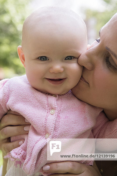 Portrait of Caucasian mother kissing cheek of baby daughter