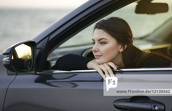 Nachdenkliche kaukasische Frau  die sich in ein Autofenster lehnt